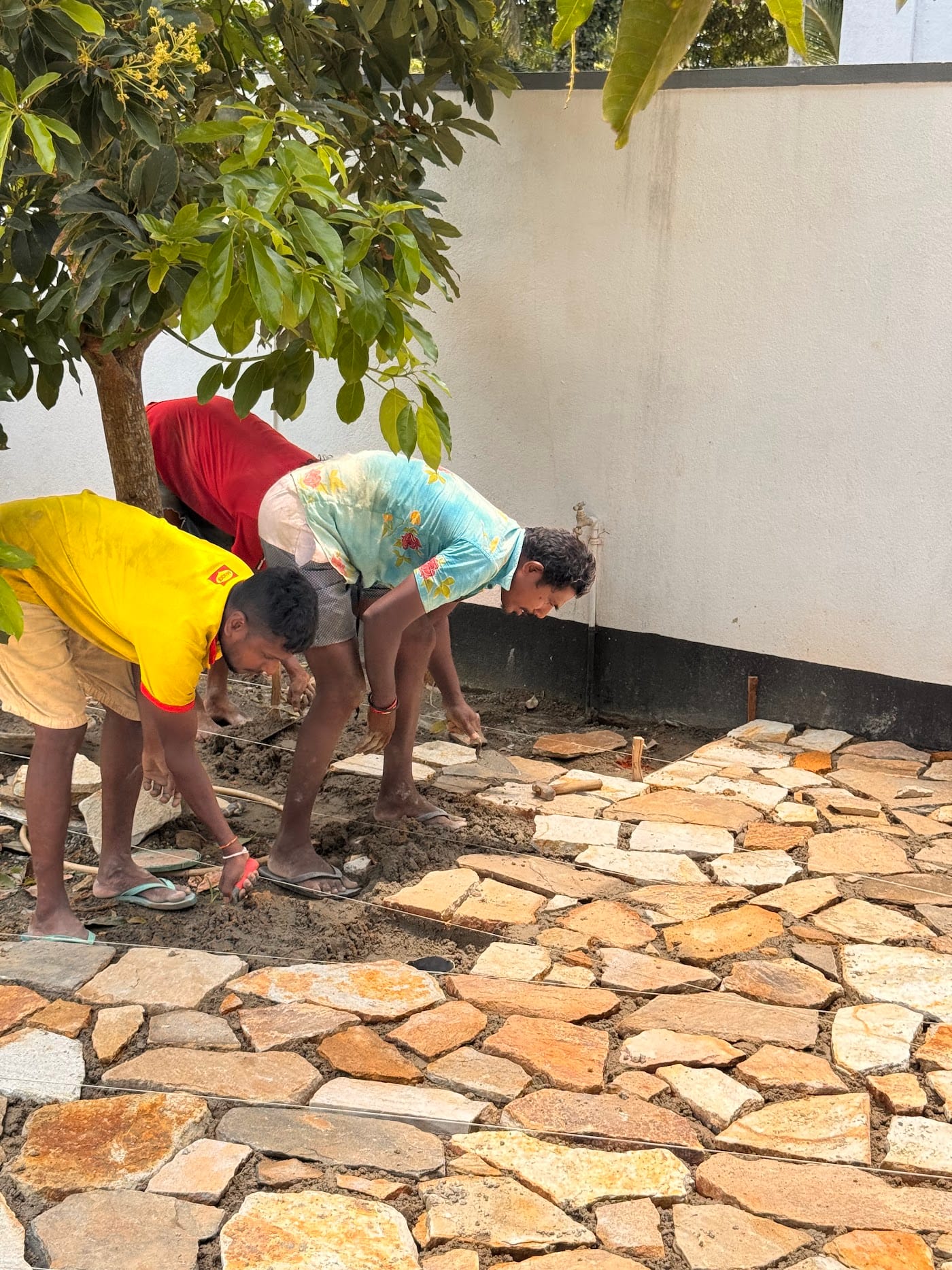 Local craftsmen laying a natural stone path in the Kelani garden in Madiha